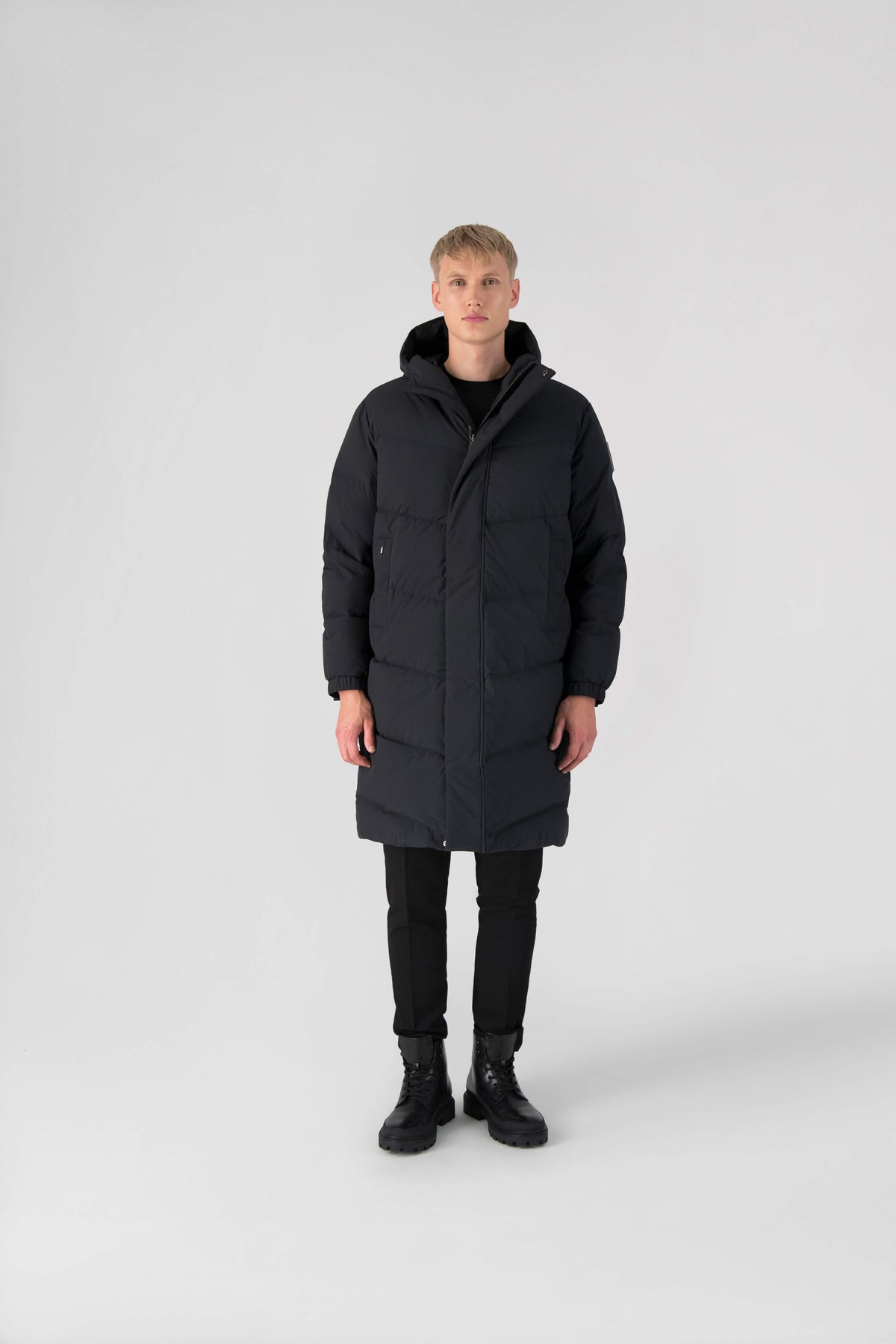 Granger long jacket in Black stretch ripstop fabric with DWR coating, insulated with Canadian white duck down and Primaloft. Features a two-way zipper, magnetic closure, and adjustable cuffs for warmth and weather protection.