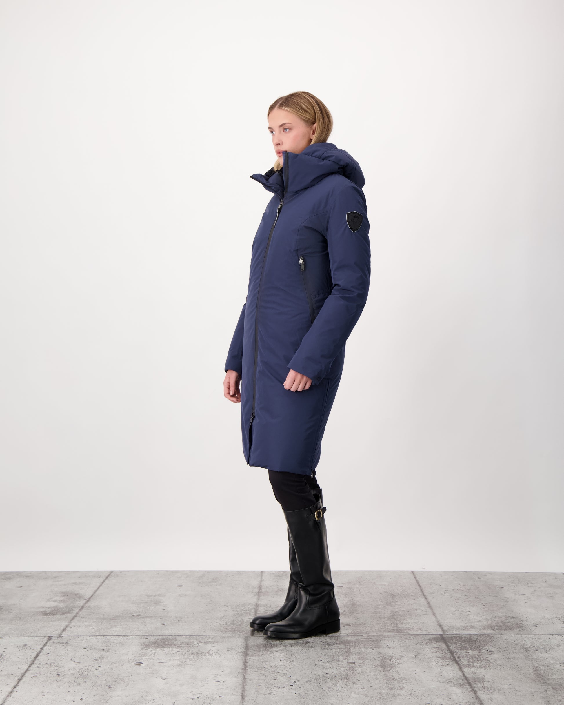 Inara Women's Performance Parka in knee length, premium 3-ply micro denier and stretch ripstop fabrication with DWR coating, Premium Canadian White Duck Down insulation, non-removable down-filled hood, centre front two-way zipper, large vertical zipper pockets along waist, zipper vents along bottom side hem, in Marine
