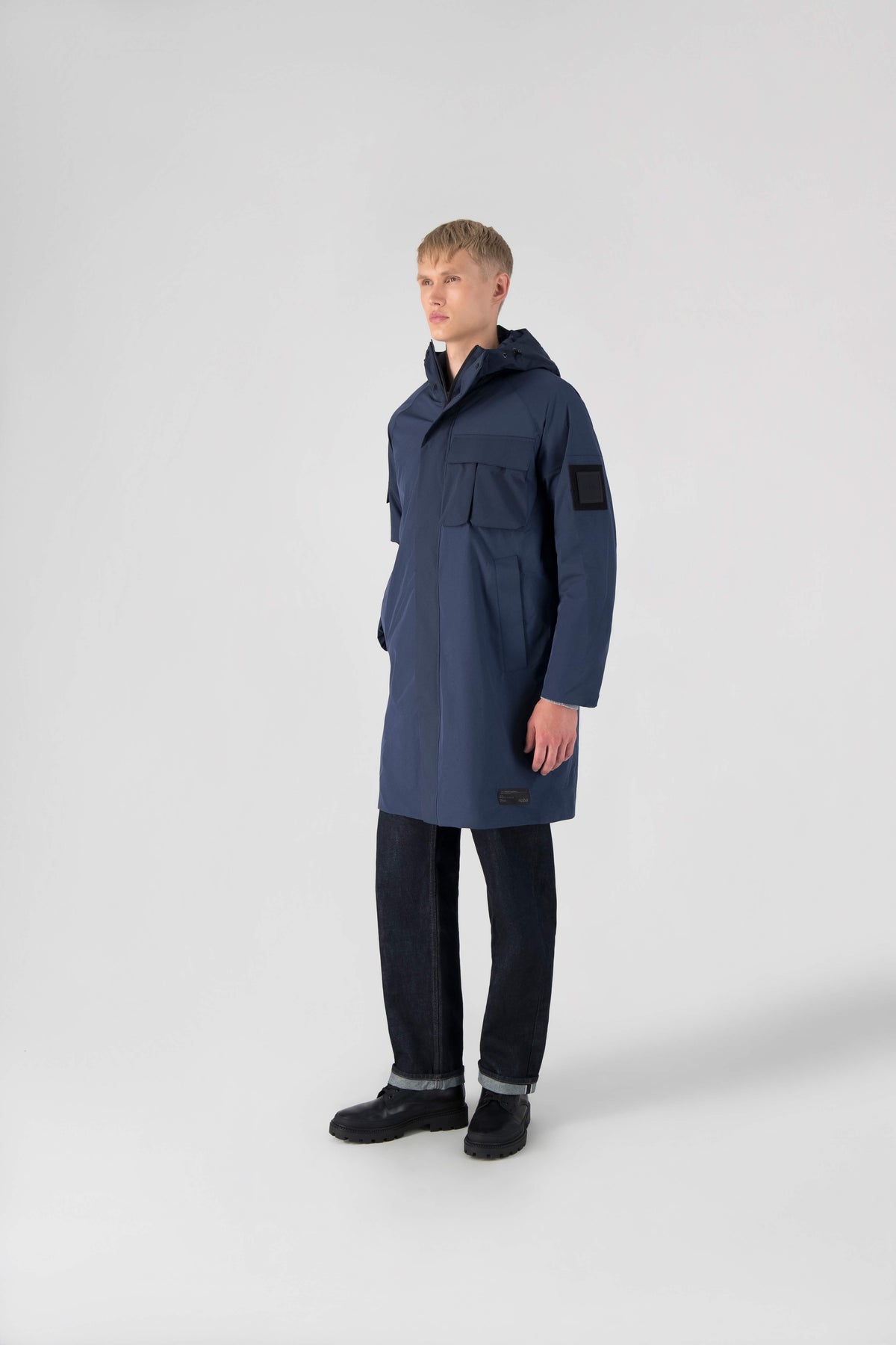 Wylder Men's Performance Rain Jacket in knee length, premium 3-ply Micro Denier and stretch ripstop fabrication, non-removable hood with reflective piping and adjustable draw cord, split utility chest pocket with magnetic flap closure, single welt pockets with magnetic closure at waist, back yoke with mesh ventilation, snap button wind flap, two-way branded zipper at centre front, telescopic sleeves with elasticized cuffs, interior draw cord at waist, in Marine