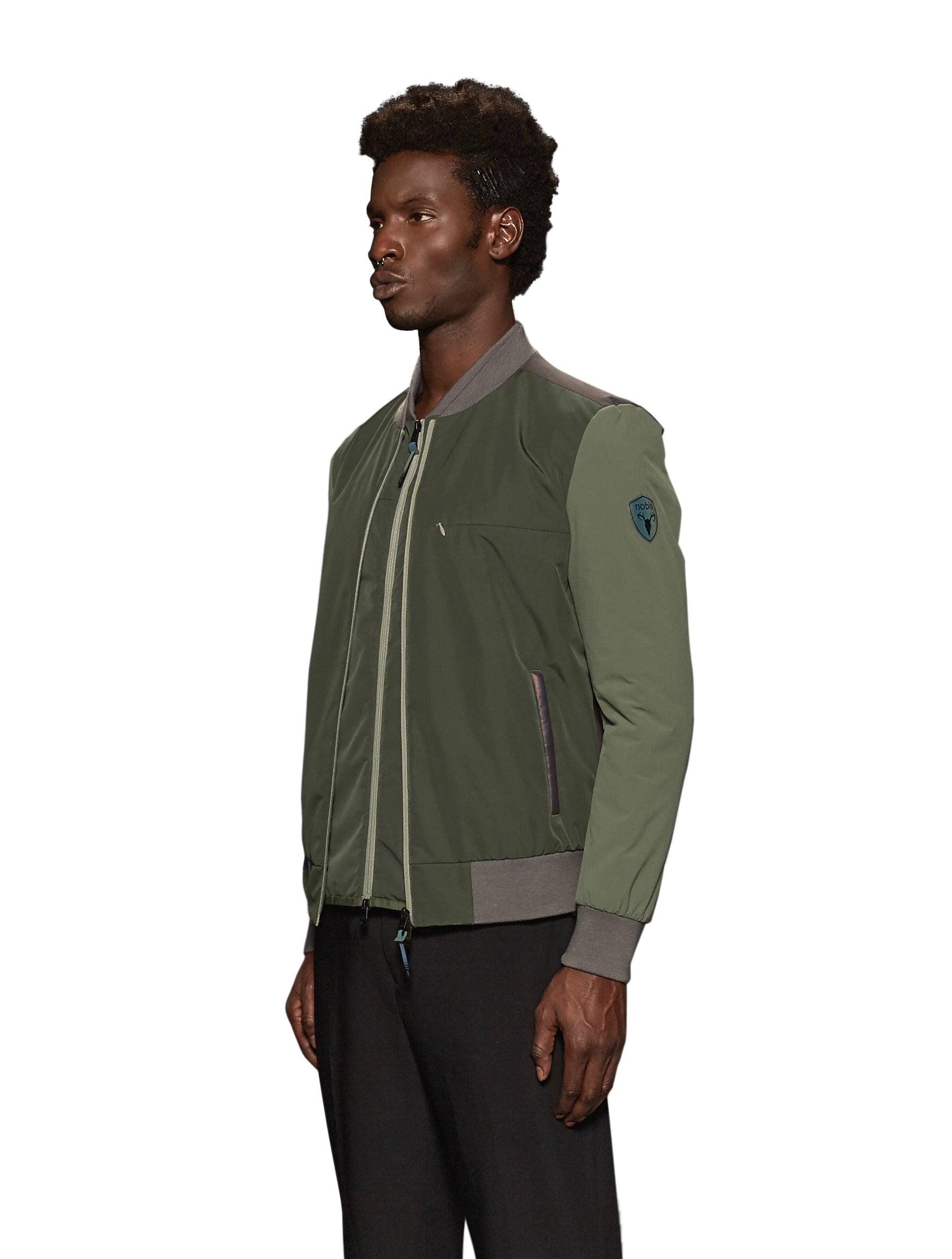 Unisex hip length bomber jacket with a contrast colour back panel, and zipper pockets at waist and an invisible zipper pocket at chest, in Dusty Olive/Licorice
